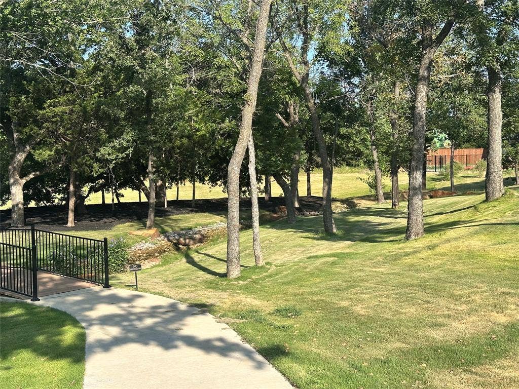 300 Park Avenue, Keller, TX 76262 Expansive green space featuring mature trees, a paved walkway, a black metal bridge, and a natural creek bed