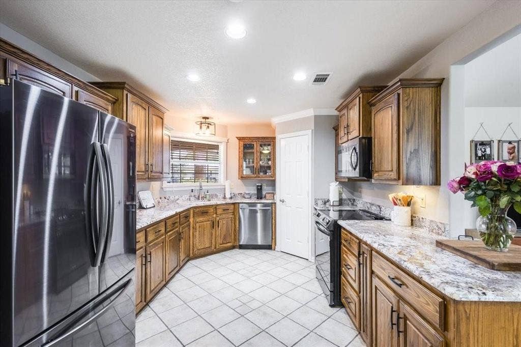 Kitchen with brown cabinets, visible vents, black range with electric stovetop, stainless steel dishwasher, and freestanding refrigerator