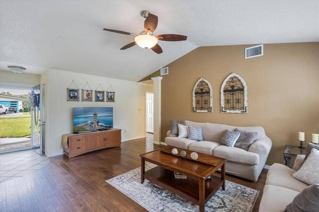 Living area with lofted ceiling, visible vents, ornate columns, and wood finished floors
