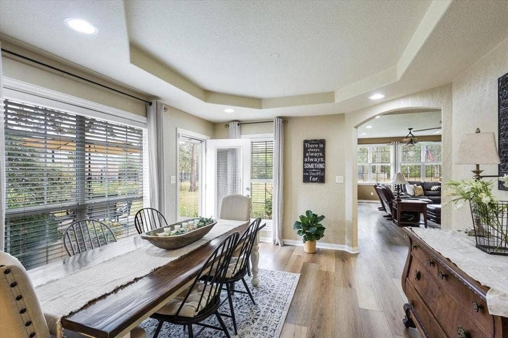Dining room with arched walkways, a textured ceiling, baseboards, light wood finished floors, and a raised ceiling