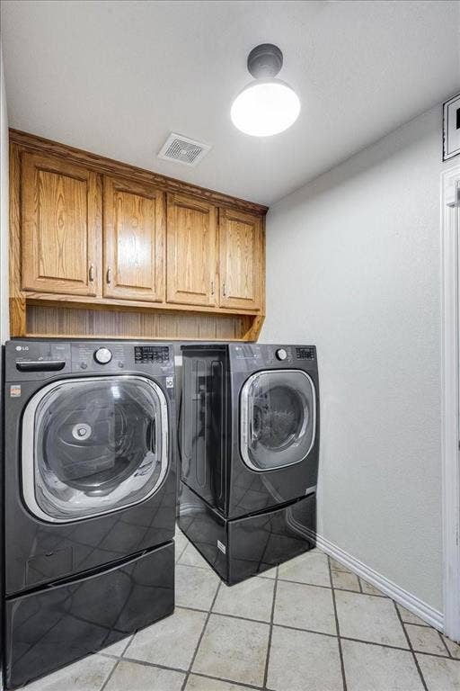 Washroom with light tile patterned flooring, washing machine and dryer, visible vents, baseboards, and cabinet space