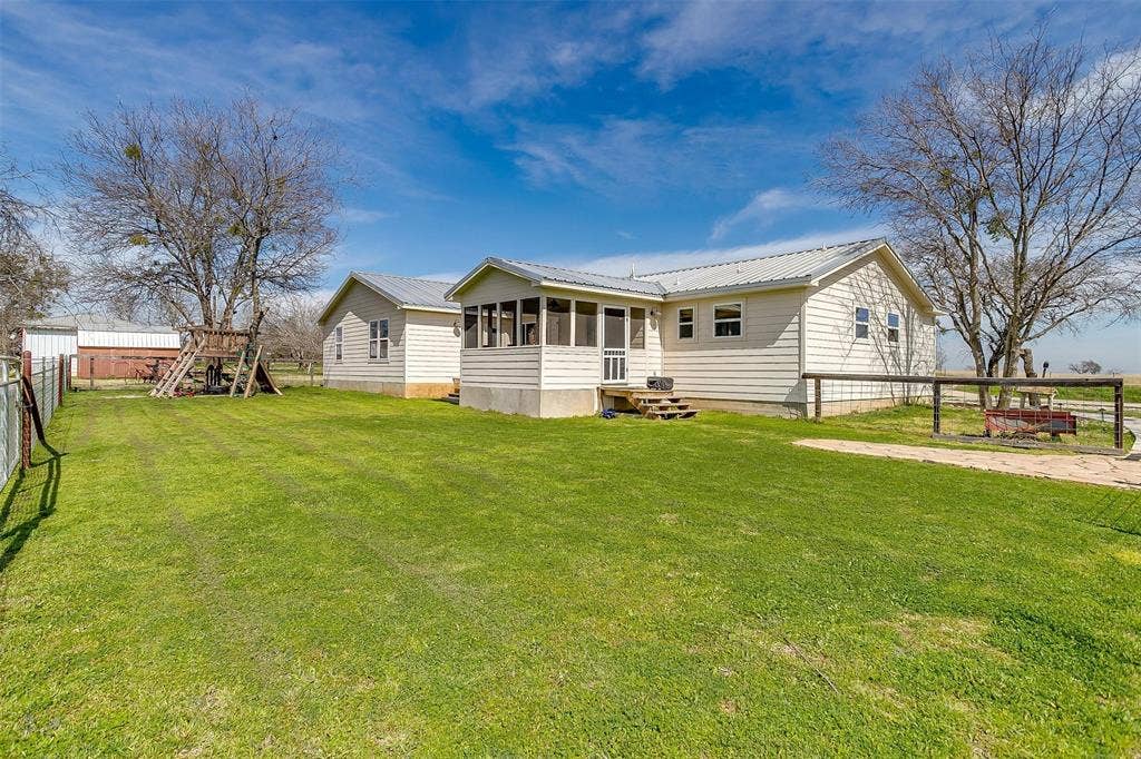 939 Twin Bends Road, Crawford, TX 76638 Back of property featuring fence, a yard, a sunroom, a playground, and metal roof