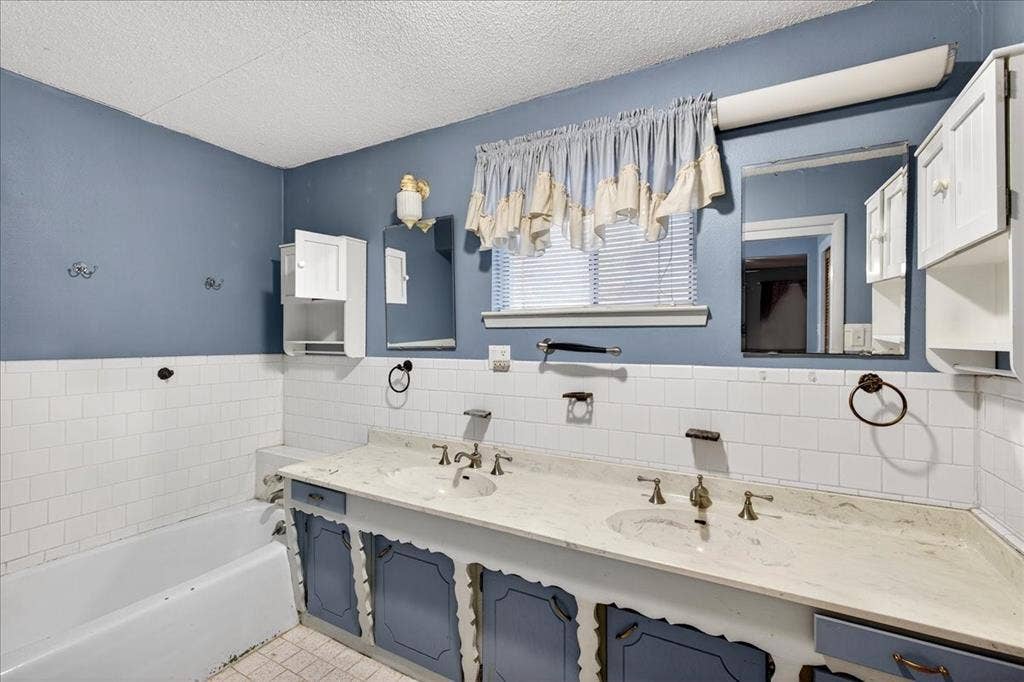 6903 Scott Street, Eustace, TX 75124 Bathroom featuring tile walls, double vanity, a bath, a textured ceiling, and a wainscoted wall