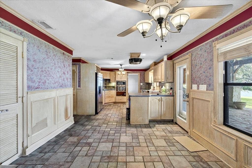 6903 Scott Street, Eustace, TX 75124 Kitchen featuring appliances with stainless steel finishes, a peninsula, wallpapered walls, light brown cabinetry, and wainscoting