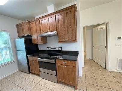 507 E Bryson Street, #A, Athens, TX 75751 Kitchen with appliances with stainless steel finishes, dark countertops, light tile patterned flooring, under cabinet range hood, and baseboards