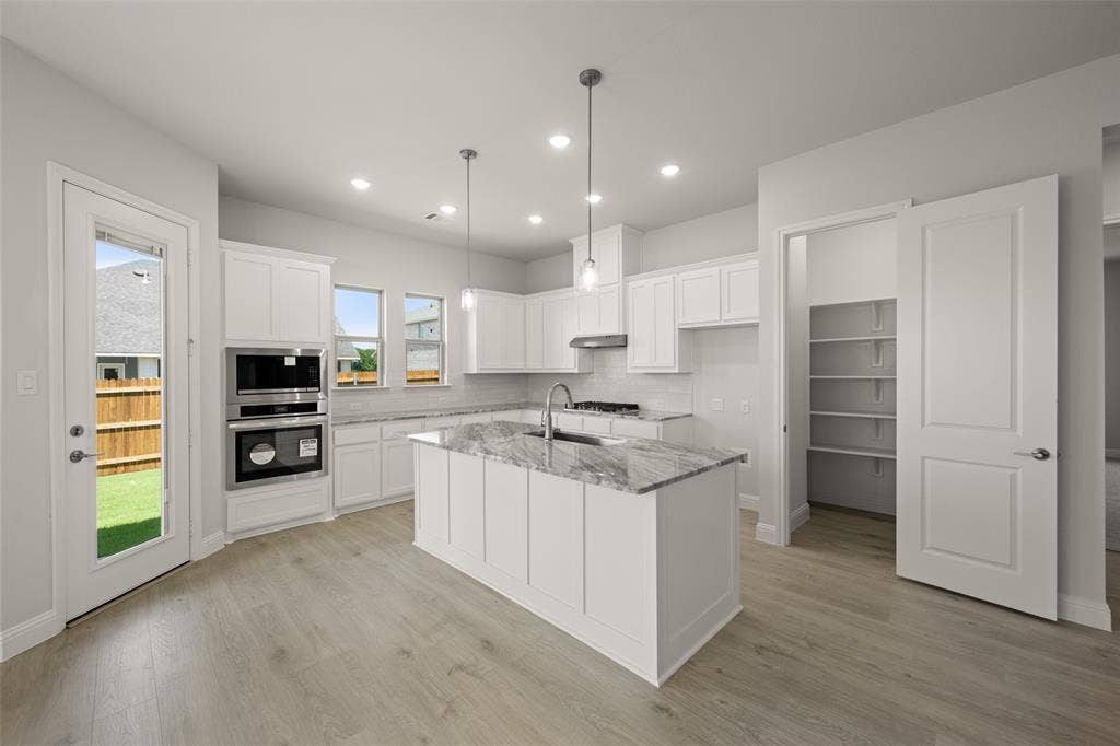 413 Wabash Drive, Waxahachie, TX 75167 Kitchen with under cabinet range hood, tasteful backsplash, light stone countertops, white cabinets, and an island with sink