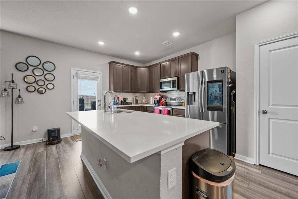 3501 Beutel Road, Waco, TX 76655 Kitchen with appliances with stainless steel finishes, decorative backsplash, light countertops, dark brown cabinets, and light wood finished floors