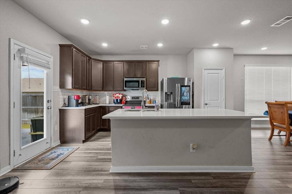 3501 Beutel Road, Waco, TX 76655 Kitchen with dark brown cabinets, appliances with stainless steel finishes, backsplash, light countertops, and an island with sink