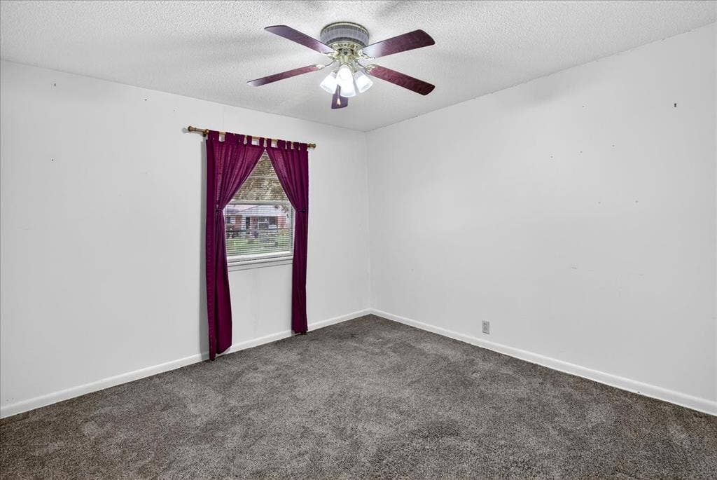 Empty room featuring dark carpet, a textured ceiling, and ceiling fan