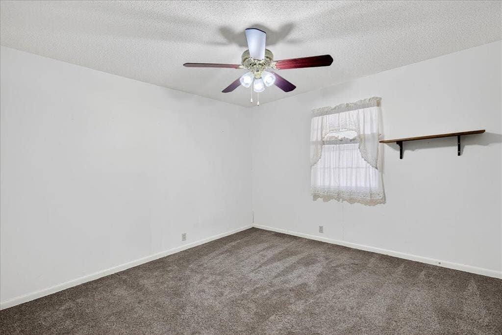 Empty room featuring dark colored carpet, a textured ceiling, and a ceiling fan