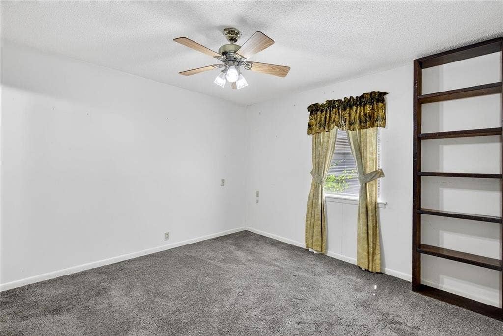 Carpeted empty room featuring a textured ceiling and a ceiling fan