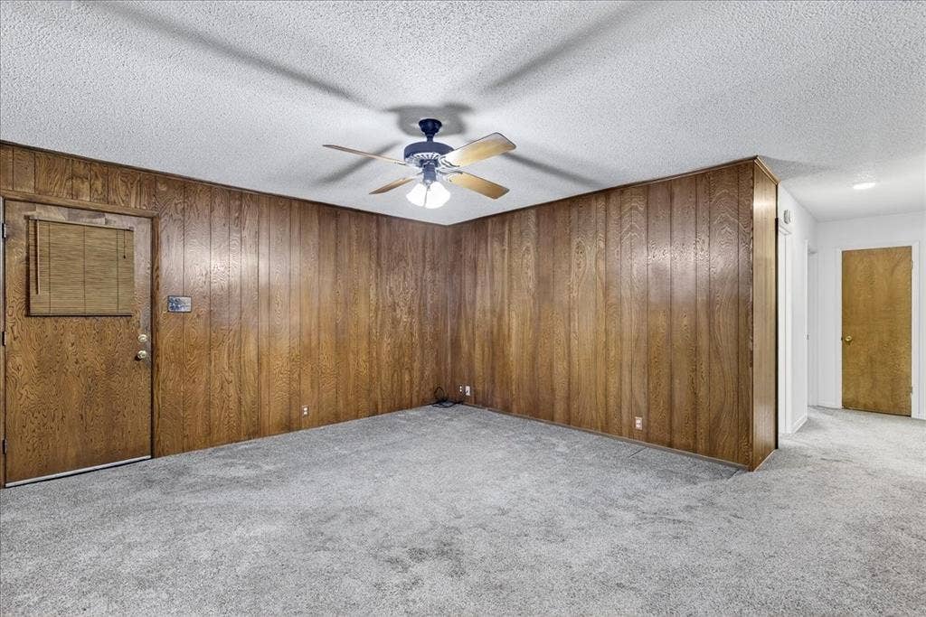 Empty room featuring light carpet, wooden walls, a textured ceiling, and a ceiling fan
