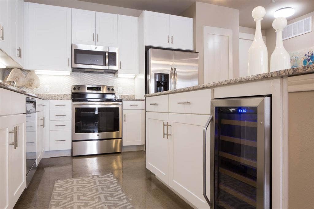 908 N Bishop Avenue, #2-103, Dallas, TX 75208 Kitchen featuring stainless steel appliances, white cabinets, wine cooler, backsplash, and light stone counters