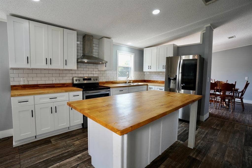 245 Oak Hill Court, Waxahachie, TX 75167 Kitchen featuring wall chimney range hood, white cabinetry, dark wood-style floors, a textured ceiling, and stainless steel appliances