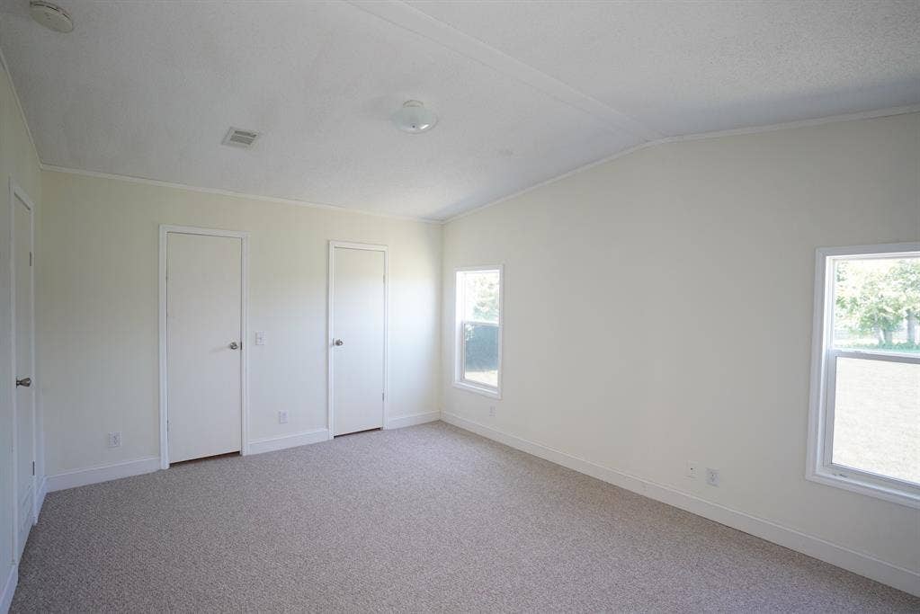 245 Oak Hill Court, Waxahachie, TX 75167 Unfurnished bedroom featuring light colored carpet, two closets, vaulted ceiling, and ornamental molding