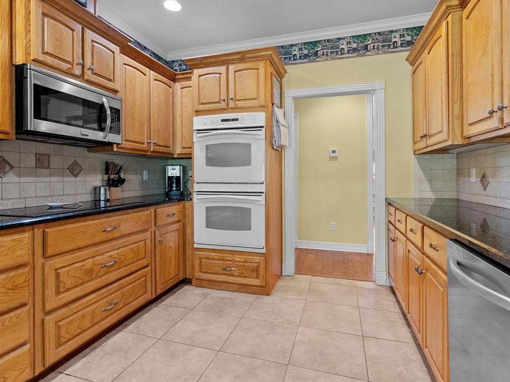 20941 Fm 16 W, Lindale, TX 75771 Kitchen featuring tasteful backsplash, stainless steel appliances, light tile patterned floors, crown molding, and dark stone countertops