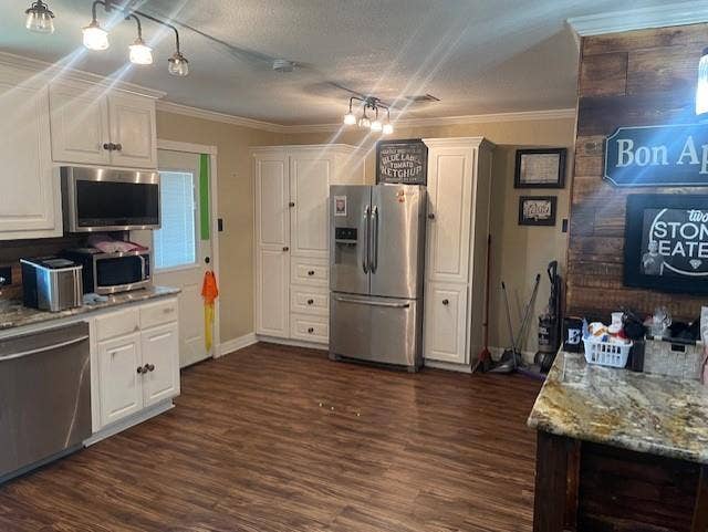 Kitchen featuring appliances with stainless steel finishes, light stone counters, crown molding, white cabinetry, and a textured ceiling