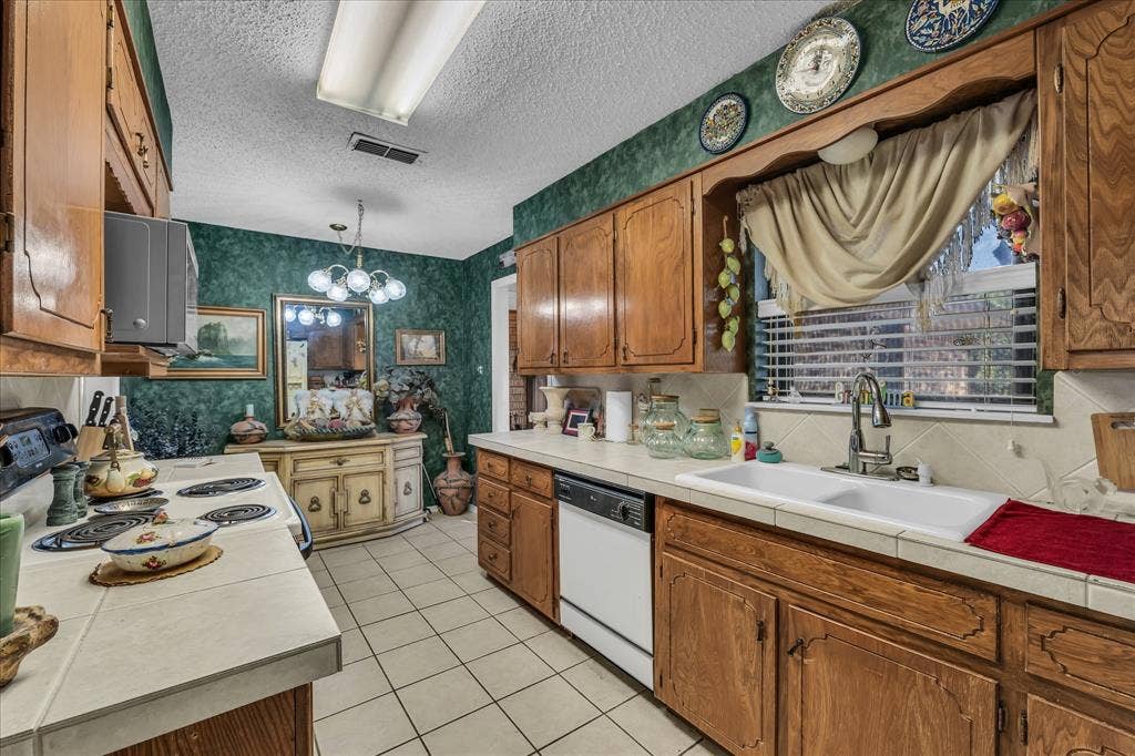 3405 Edna Avenue, Waco, TX 76708 Kitchen featuring wallpapered walls, brown cabinetry, tile countertops, pendant lighting, and white appliances
