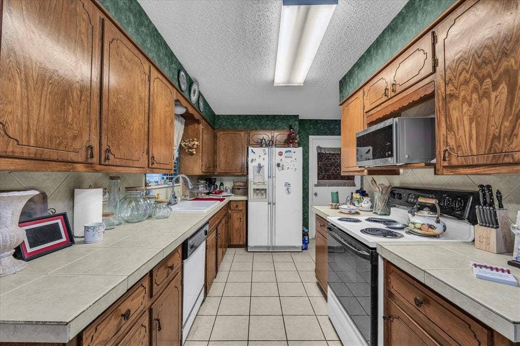 3405 Edna Avenue, Waco, TX 76708 Kitchen featuring white appliances, brown cabinetry, light tile patterned flooring, a textured ceiling, and backsplash