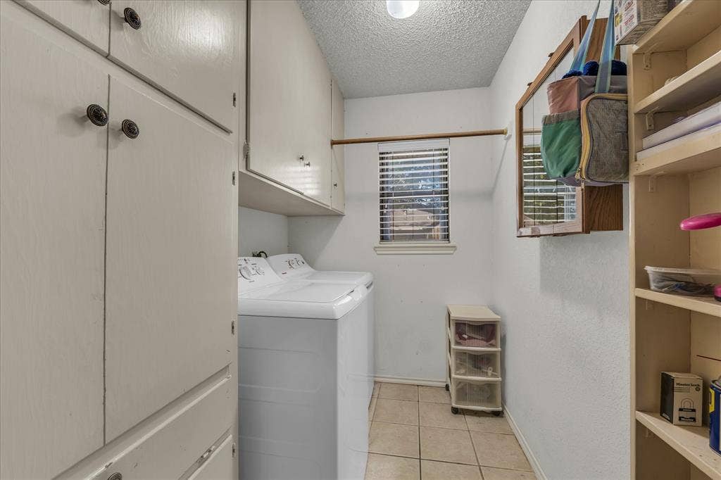 3405 Edna Avenue, Waco, TX 76708 Washroom with light tile patterned floors, a textured ceiling, washing machine and clothes dryer, and cabinet space