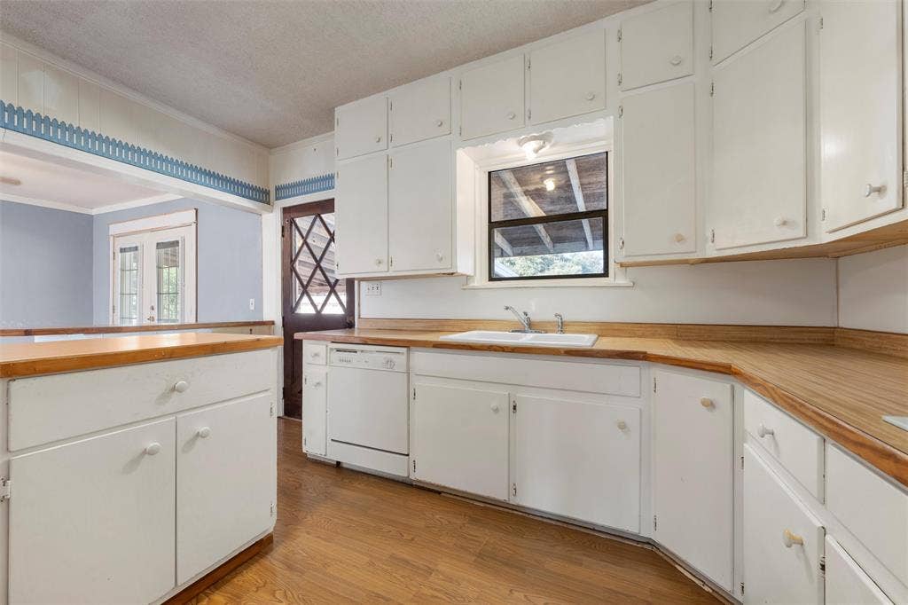 12145 Tree Lake Drive, Waco, TX 76708 Kitchen with light countertops, crown molding, light wood-type flooring, white dishwasher, and white cabinetry