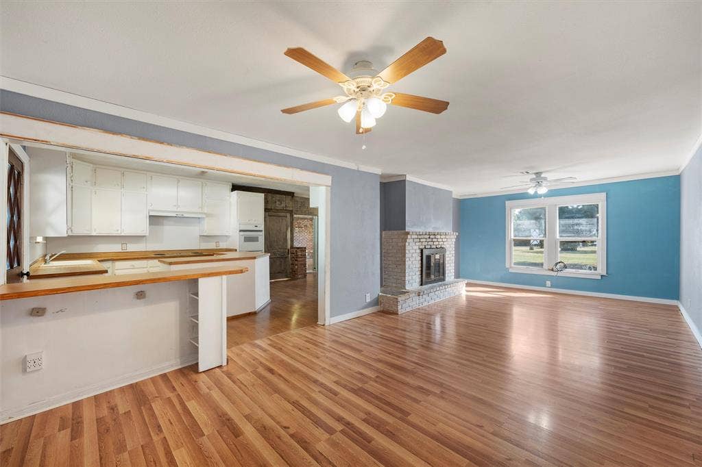 12145 Tree Lake Drive, Waco, TX 76708 Unfurnished living room featuring light wood-style floors, ornamental molding, ceiling fan, and a fireplace