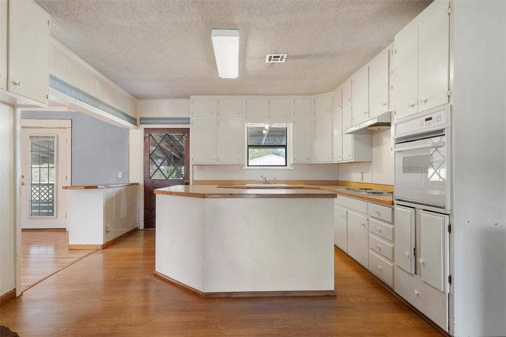 12145 Tree Lake Drive, Waco, TX 76708 Kitchen with a textured ceiling, white cabinets, a kitchen island, light wood-type flooring, and light countertops