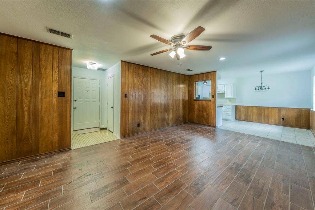 105 Briar Lane, Waxahachie, TX 75165 Unfurnished living room with wood walls, a wainscoted wall, wood finish floors, ceiling fan, and a chandelier