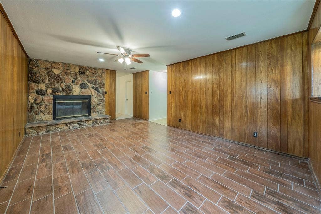 105 Briar Lane, Waxahachie, TX 75165 Unfurnished living room featuring wooden walls, a stone fireplace, a ceiling fan, and dark wood-style floors