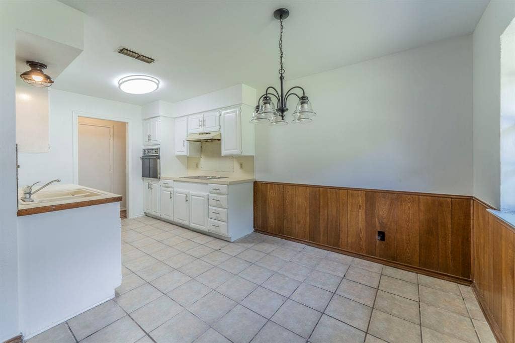 105 Briar Lane, Waxahachie, TX 75165 Kitchen with white cabinets, wooden walls, a wainscoted wall, light countertops, and light tile patterned floors