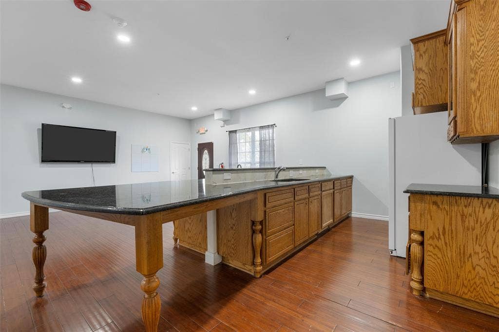 Kitchen with brown cabinets, freestanding refrigerator, dark wood-style floors, dark stone counters, and recessed lighting