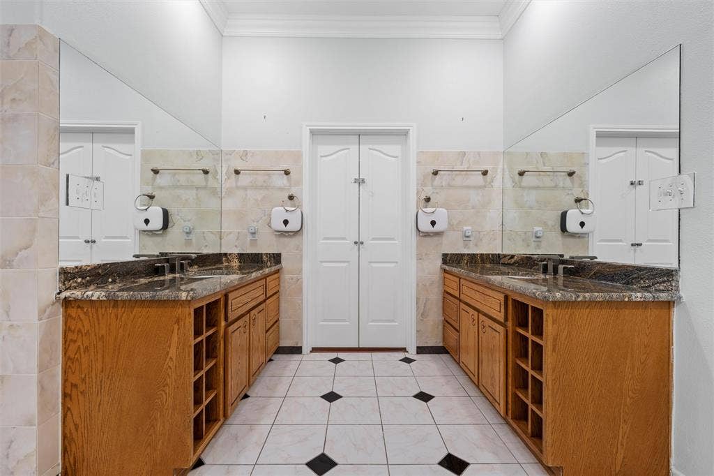 Bathroom with tile walls, two vanities, light tile patterned floors, crown molding, and a closet