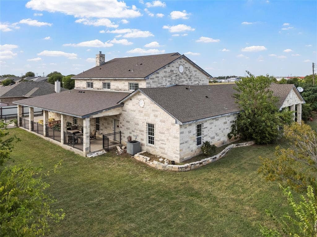 Back of house with a chimney, a patio, a lawn, and stone siding
