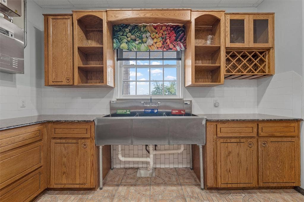Kitchen with open shelves, brown cabinets, dark stone countertops, and decorative backsplash