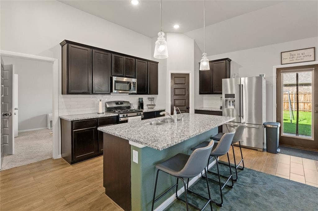 Kitchen with decorative backsplash, stainless steel appliances, dark brown cabinetry, decorative light fixtures, and lofted ceiling