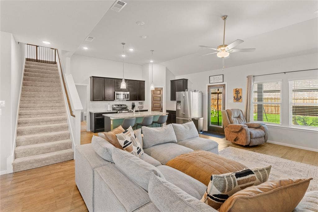 Downstairs living room with stairs, light wood-type flooring, lofted ceiling, ceiling fan, and recessed lighting