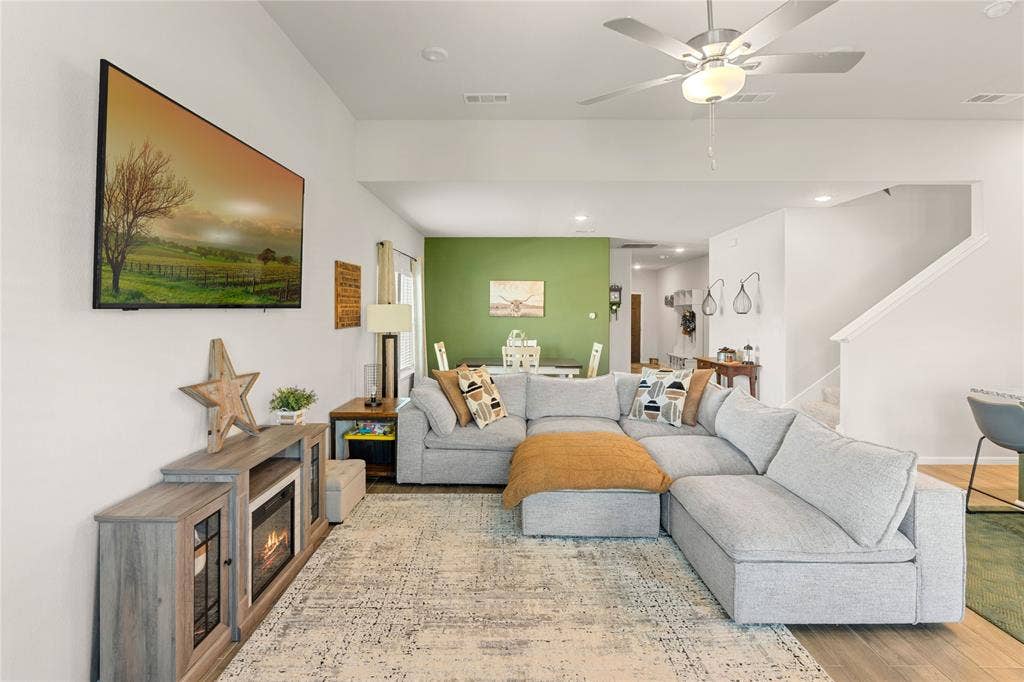 Spacious living area with wood finished floors, accent wall, ceiling fan, stairs, and recessed lighting