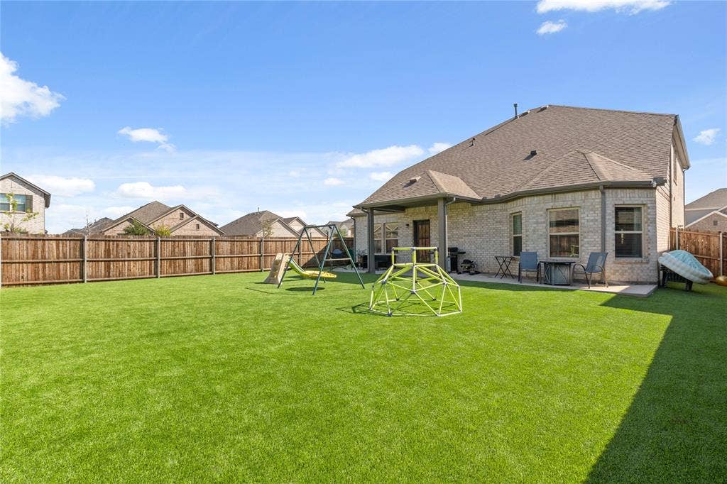Rear view of house with a spacious fenced backyard, a shingled roof, a patio area, a playground, and brick siding