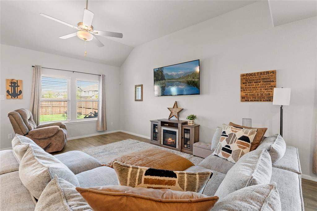 Downstairs living room featuring wood finished floors, a glass covered fireplace, lofted ceiling, and a ceiling fan