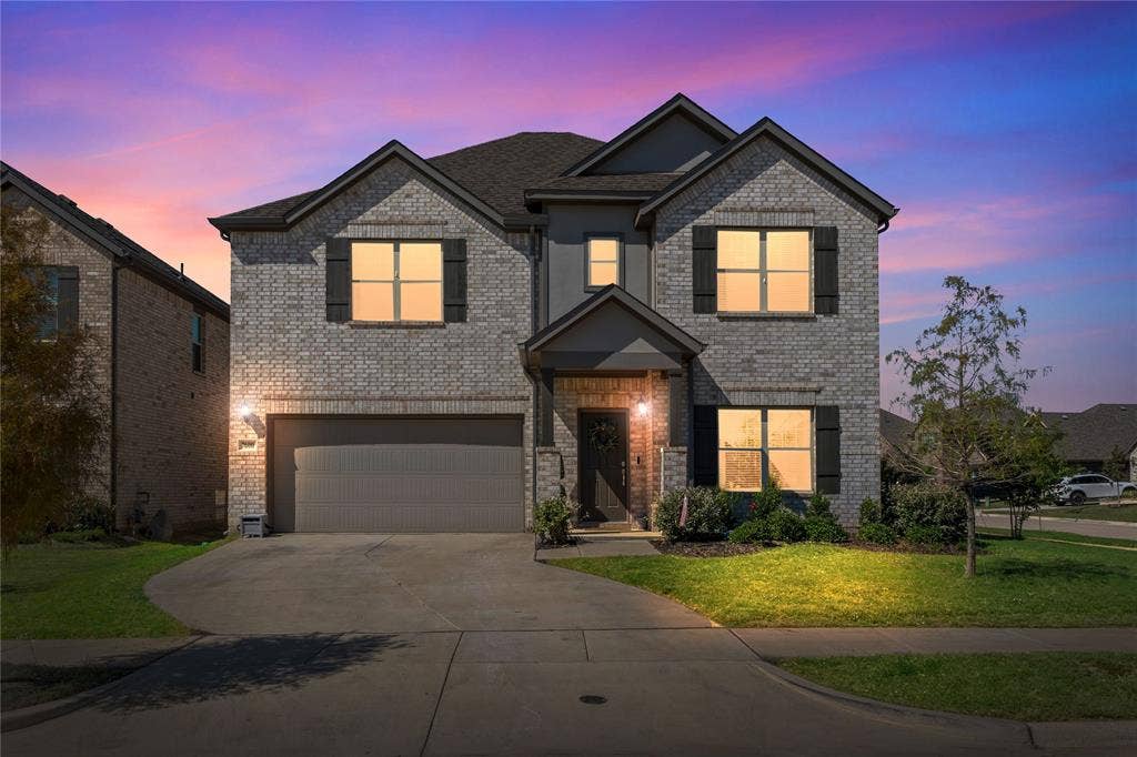 Twilight view of front of property with a yard, concrete driveway, brick siding, and a garage