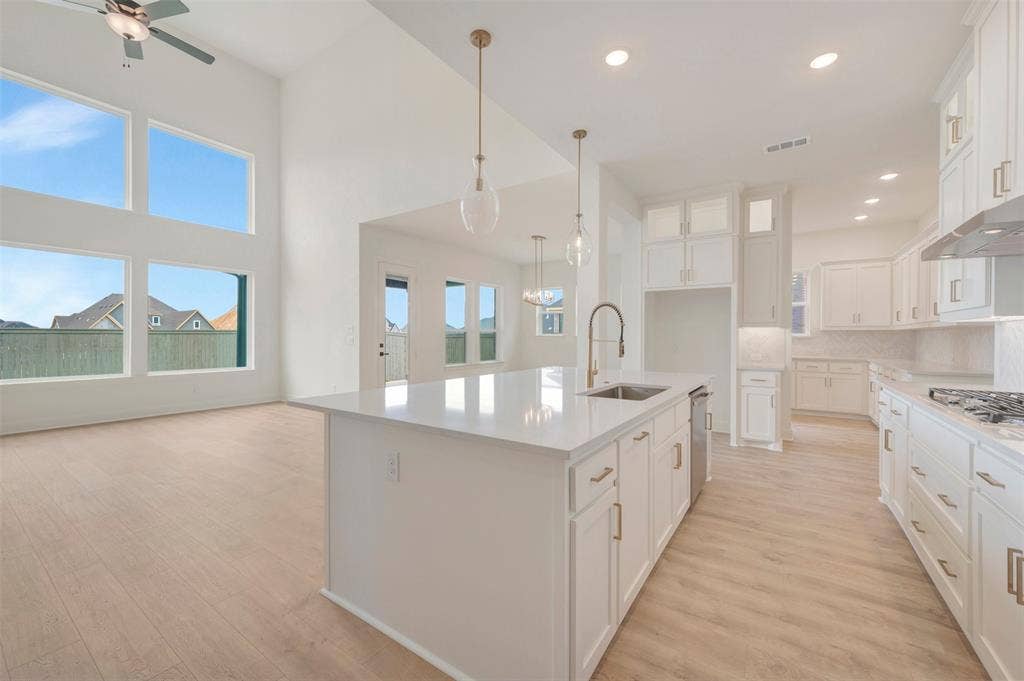 Open-concept living space featuring a kitchen island with sink and stainless steel dishwasher, white cabinetry with gold-finish hardware, recessed lighting, and wood-finish flooring
