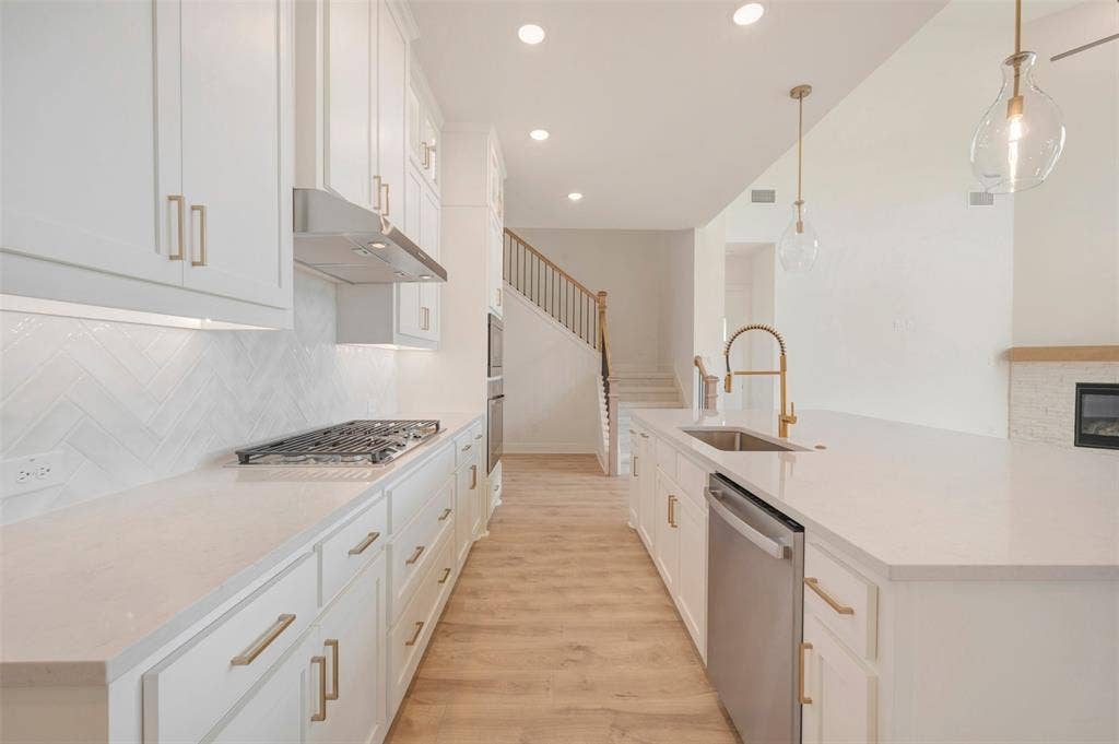 Contemporary kitchen featuring white cabinetry with brass hardware, a gas range with stainless steel hood, and a herringbone tile backsplash