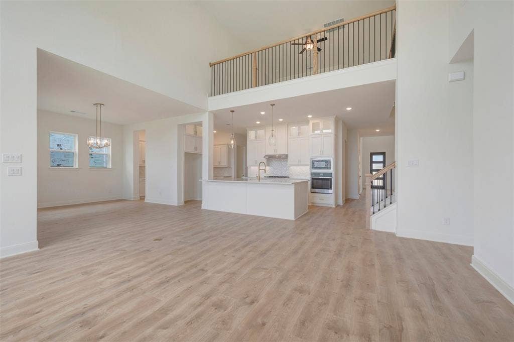Spacious interior featuring wood-finish flooring, a two-story ceiling, and an open-concept kitchen with white cabinetry and an island