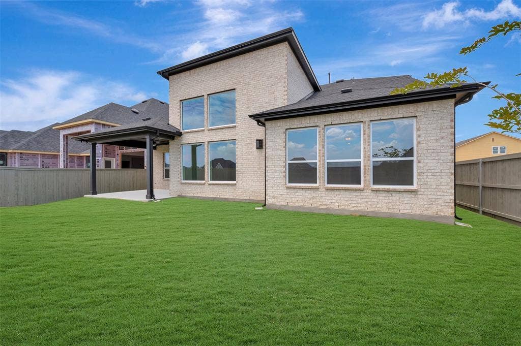 Spacious rear yard with a covered patio, expansive lawn, and light-colored brick exterior