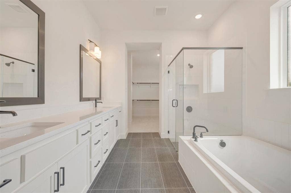 Contemporary bathroom featuring a double vanity with stone countertops, a freestanding bathtub, and a glass-enclosed shower