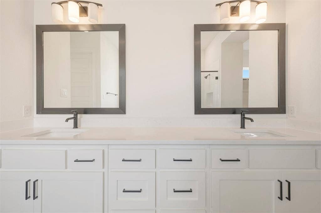 Dual vanities featuring white cabinetry with matte black hardware, integrated sinks, and light-toned countertops