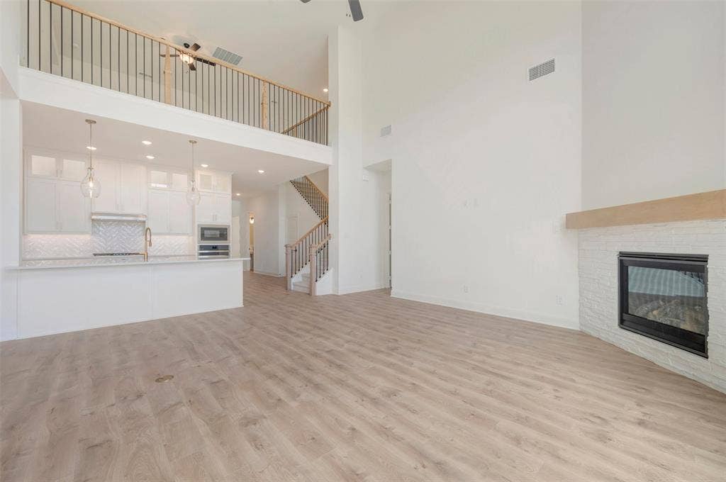 Spacious living area featuring wood-finish flooring, a white brick fireplace with a wood mantle, and high ceilings