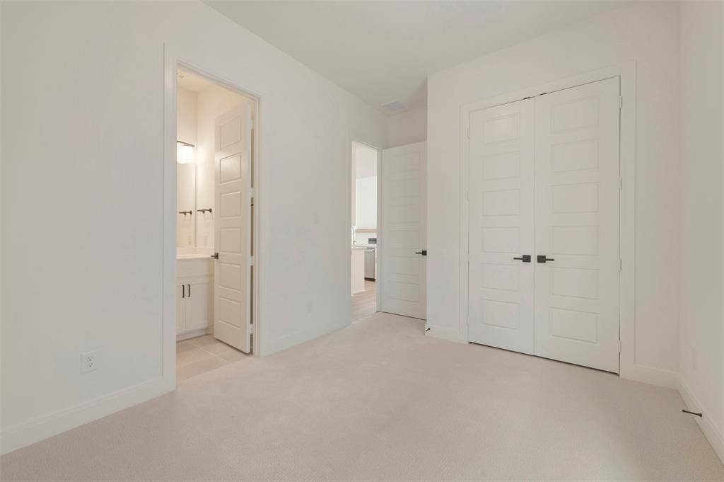 Carpeted room featuring white walls, white baseboards, and a double-door closet with matte black hardware