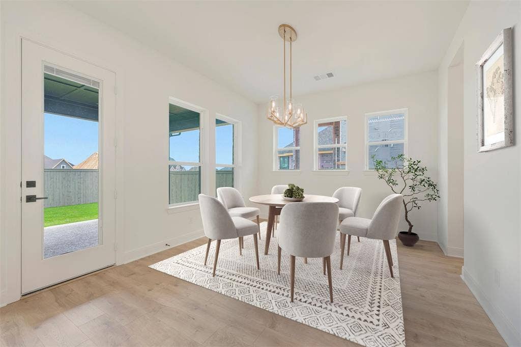 Bright dining area featuring wood-finish flooring, multiple windows, a full-light glass door, and a contemporary gold-tone chandelier