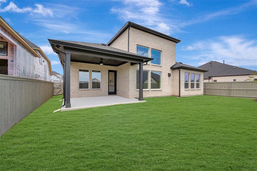 Spacious backyard featuring a covered patio, extensive lawn, multi-pane windows, brick exterior, and a solid privacy fence